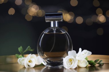 Bir şişe aromatik parfüm ve metal tepside çiçeklerle siyah arka planda bulanık ışıklar, yakın plan. Bokeh etkisi