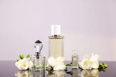 Ayna yüzeyinde açık gri arka plana karşı aromatik parfüm şişeleri ve çiçekler