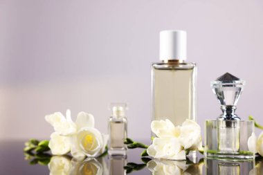 Ayna yüzeyinde açık gri arkaplana karşı aromatik parfüm şişeleri ve çiçekler, yakın plan