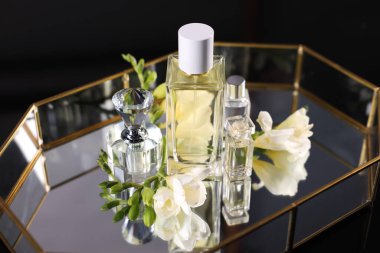 Siyah arka plan karşısında şık tepside aromalı parfüm şişeleri ve çiçekler.