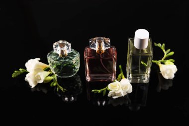 Siyah ayna yüzeyinde aromatik parfüm şişeleri ve çiçekler
