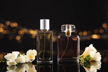 Ayna yüzeyinde aromatik parfüm şişeleri ve çiçekler bulanık ışıklarla siyah arka plana karşı, yakın plan. Bokeh etkisi