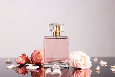 Ayna yüzeyinde bir şişe aromatik parfüm ve çiçek Gri arka planda, yakın plan