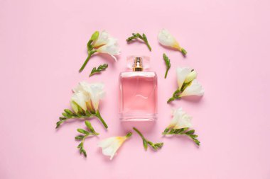 Bir şişe parfüm ve pembe arka planda güzel çiçekler.