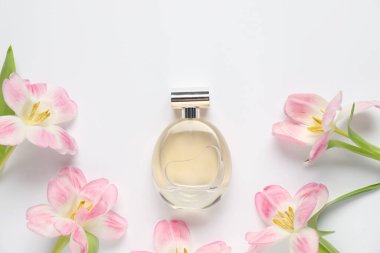Bir şişe parfüm ve beyaz arka planda güzel çiçekler.