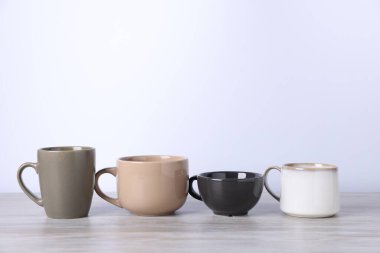 Beyaz arka plana karşı açık ahşap masada bir sürü renkli fincan var. Metin için boşluk