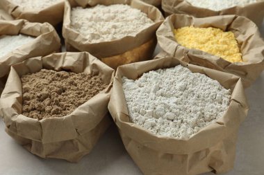 Beyaz masadaki kağıt torbalarda farklı türde un, yakın plan.