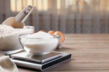 Dijital mutfak terazisi, bir kase şeker ve ahşap masa üzerindeki diğer ürünler, yakın plan. Metin için boşluk