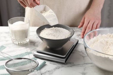 Beyaz mermer masadaki dijital mutfak terazisine şeker koyan kadın, yakın plan.