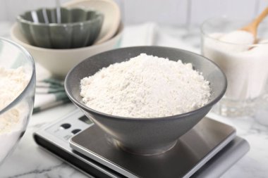 Dijital mutfak terazisi, beyaz mermer masa üzerinde bir kase un ve diğer ürünler, yakın plan.