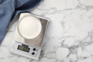 Dijital mutfak terazisi, beyaz mermer masa üzerinde bir bardak şeker, üst manzara. Metin için boşluk