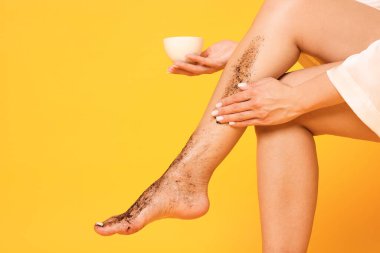 Turuncu arka planda bacağına vücut masajı yapan bir kadın. Yakın plan. Metin için boşluk