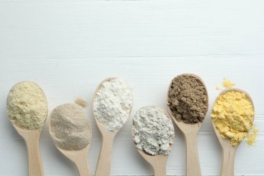 Beyaz ahşap masadaki kaşıklarda farklı türde un, düz. Metin için boşluk