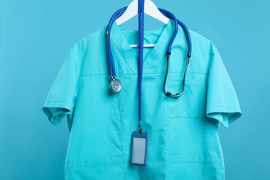 Steteskop ve rozetli sağlık çalışanı üniforması mavi arka planda.
