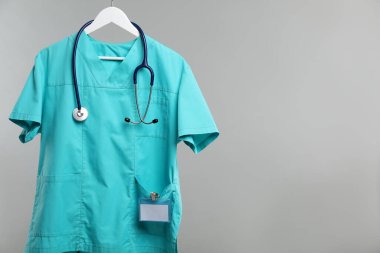 Steteskop ve rozetli sağlık çalışanı üniforması gri arka planda. Metin için boşluk