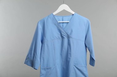 Sağlık çalışanı üniforması gri arkaplanda asılı.