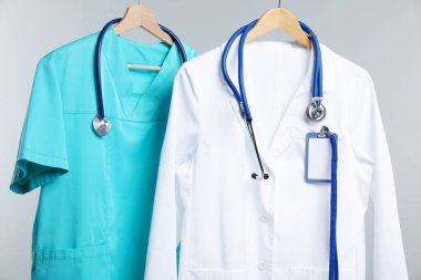 Steteskop ve rozetli sağlık görevlileri gri arkaplanda asılı.