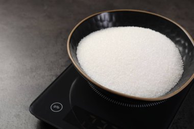 Dijital mutfak terazisi, gri masada bir kase şeker, yakın plan.