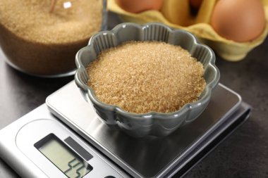 Dijital mutfak terazisi, kahverengi şeker kasesi ve gri masadaki diğer ürünler, yakın plan.