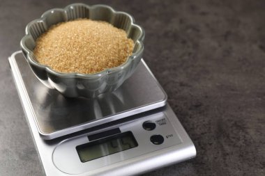 Dijital mutfak terazisi ve gri masada bir kase kahverengi şeker, yakın plan. Metin için boşluk