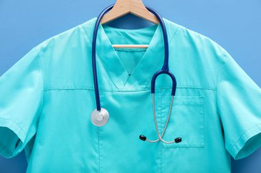 Mavi arka planda steteskop takılı sağlık görevlisi üniforması, yakın plan.