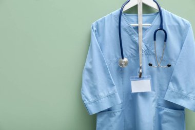 Steteskop ve rozeti açık yeşil arka planda asılı sağlık görevlisi üniforması. Metin için boşluk