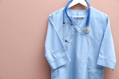 Bej arka planda steteskop takılı sağlık çalışanı üniforması. Metin için boşluk