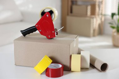 Yapışkan bant ruloları ve kapalı masa üzerindeki karton kutuyla birlikte dağıtıcı.