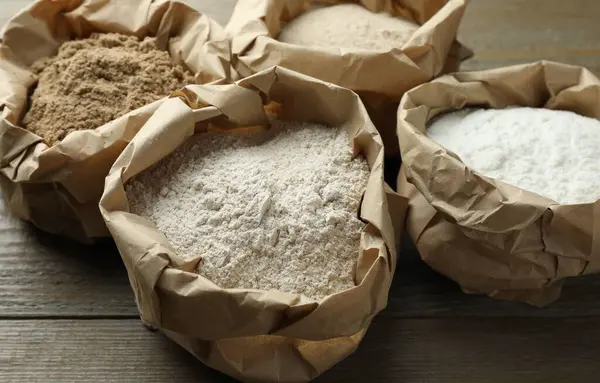 Tahta masadaki kağıt torbalarda farklı türde un, yakın plan.