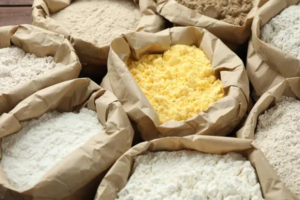 Tahta masadaki kağıt torbalarda farklı türde un, yakın plan.