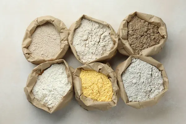 Beyaz masadaki kağıt torbalarda farklı türde un, düz yerde.