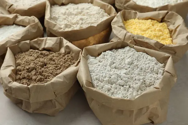 Beyaz masadaki kağıt torbalarda farklı türde un, yakın plan.