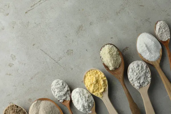 Açık gri masadaki kaşıklarda farklı türde un, düz. Metin için boşluk