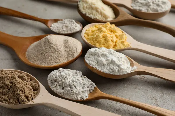 Açık gri masada kaşıklarda farklı türde un, yakın plan.