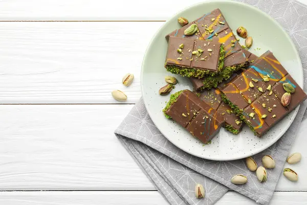 Dubai çikolatası parçaları, beyaz ahşap masa üzerinde şam fıstığı ve knafeh, düz yatıyordu. Metin için boşluk