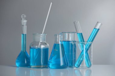 Aynanın yüzeyinde gri arka planda mavi sıvı bulunan laboratuvar camları