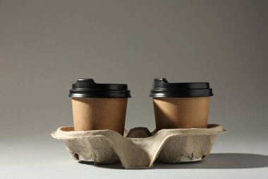 Paper coffee cups in cardboard holder on light grey background. Space for text