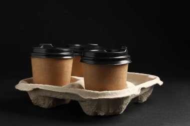 Kağıt kahve bardakları siyah arka planda karton tutucu, yakın plan.