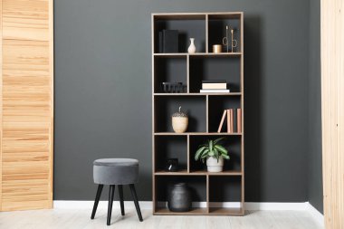 Shelving unit with decor, stool and folding screen near grey wall indoors