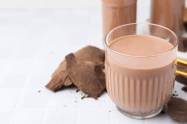 Bardakta çikolatalı süt ve beyaz fayanslı masada çikolata parçaları, yakın plan. Metin için boşluk