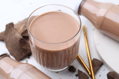 Bardakta çikolatalı süt, beyaz fayanslı masada şişeler ve çikolata parçaları, yakın plan.