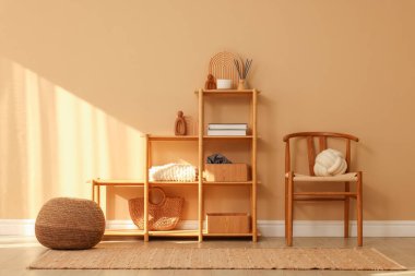 İçerideki bej duvarın yanında dekor, sandalye ve puf bulunan raf ünitesi.