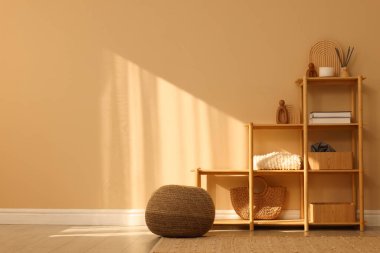 Dekorlu raf ünitesi, sandalye ve pouf kapalı alanda bej duvar, metin için boşluk