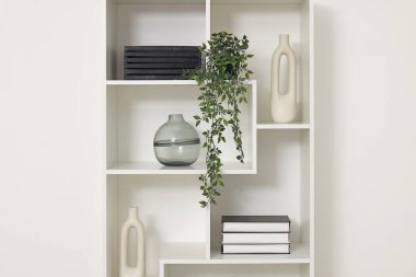 Beyaz duvarın yanında dekorlu raf ünitesi.