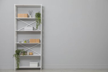 Açık gri duvarın yanındaki raflarda farklı eşyalar var. Metin için boşluk