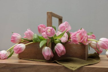 Güzel laleler sepetin içinde ahşap masada, gri arka planda, yakın planda.