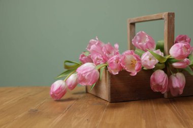 Açık yeşil arka plan karşısında sepetteki güzel laleler ahşap masada, yakın plan. Metin için boşluk