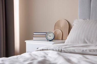 Yatağın yanında kitap, dekor ve alarmlı bir masa var.