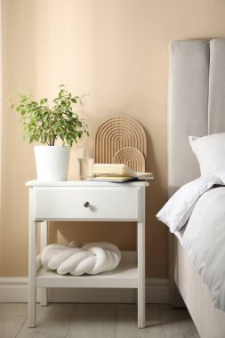 Yatağın yanında kitap, dekor ve bir bardak su olan komodin.