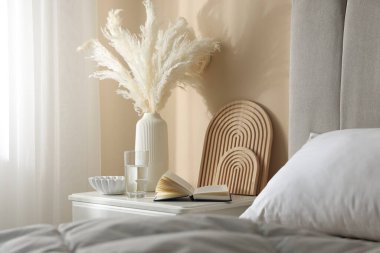 Yatağın yanında kitap, dekor ve bir bardak su olan komodin.